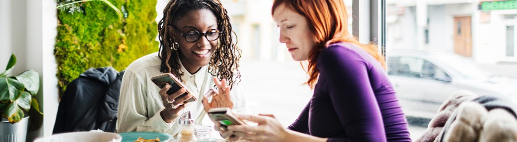 Two women consuming media on their mobile devices which Nielsen's media planning tools help measure.